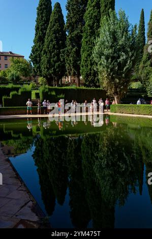 I visitatori ammirano la tranquilla piscina riflettente circondata da lussureggianti giardini e torreggianti cipressi nell'Alhambra Foto Stock