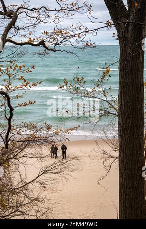Union Pier, Michigan - tre persone su una spiaggia deserta a novembre guardano le onde sul lago Michigan. Foto Stock