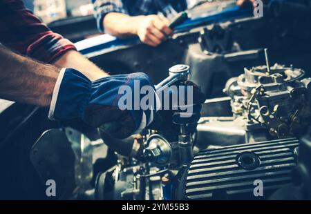 Due meccanici si concentrano sulla riparazione del motore di un'auto, utilizzando vari attrezzi per l'attività in un'officina ben attrezzata durante le ore diurne. Foto Stock