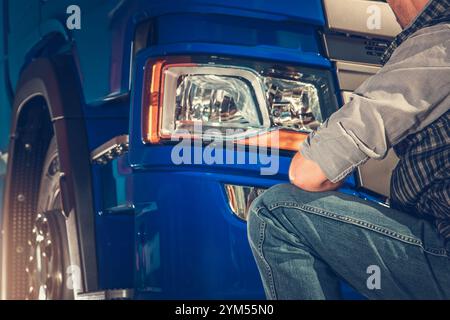 Un meccanico ispeziona e lavora sul complessivo luce anteriore di un veicolo industriale blu in un centro di assistenza ben illuminato, concentrandosi sui dettagli di riparazione e sull'attrezzatura n Foto Stock