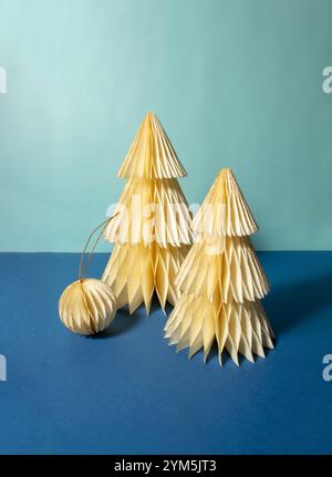 Alberi di Natale beige festivi di diverse dimensioni creati con carta con sfondo blu. Decorazioni minimaliste creative per le vacanze invernali. Foto Stock
