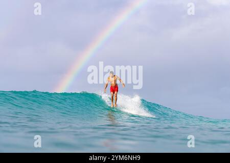 Un uomo sta navigando su un'onda con un arcobaleno sullo sfondo. La scena è un'emozione Foto Stock