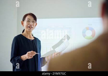 Donna giapponese anziana che fa una presentazione in ufficio Foto Stock