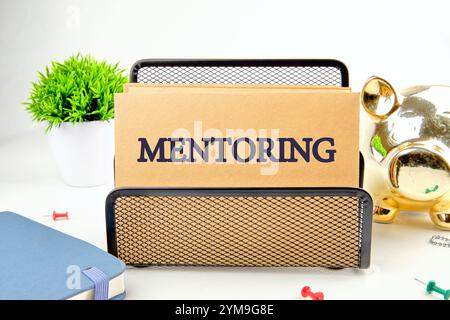 Concetto di business. Frase, testo, parole MENTORING sono scritte su carta in un supporto nero su uno sfondo chiaro. Foto Stock