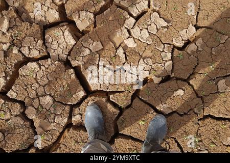 Camminare con gli stivali sul fondo incrinato di uno stagno essiccato Foto Stock