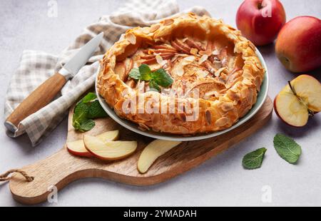 galette di mele appena sfornata decorata con scaglie di mandorle e menta, servita su un tavolo con mele fresche e un coltello Foto Stock