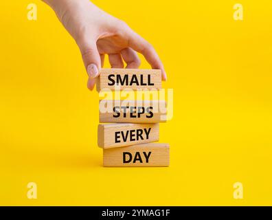 Simbolo piccoli passi ogni giorno. Blocchi di legno con parole piccoli passi ogni giorno. Bellissimo sfondo giallo. Mano d'affari. Business e piccoli passi Foto Stock