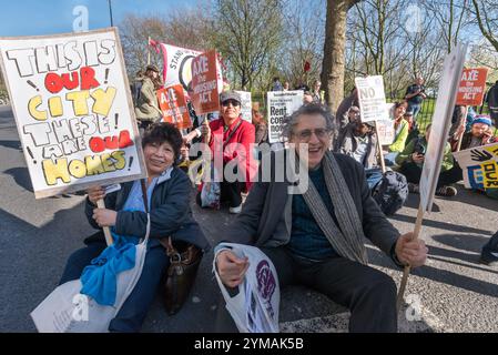 Londra, Regno Unito. 25 marzo 2017. Gli attivisti di Southwark, tra cui Piers Corbyn (centro), si siedono sulla strada principale di fronte alla Thurlow Lodge Community Hall sulla Aylesbury Estate alla fine della marcia, invitando il Consiglio laburista di Southwark a salvare case e posti di lavoro nel quartiere. La marcia era stata pianificata per terminare al Divine Rescue Homeless Charity nella sala della comunità, salvata dallo sfratto da un'occupazione da parte di attivisti all'inizio di quest'anno, ma il Consiglio di Southwark ha detto all'ente caritatevole che sarebbero stati sfrattati se avessero cooperato con la marcia. Foto Stock