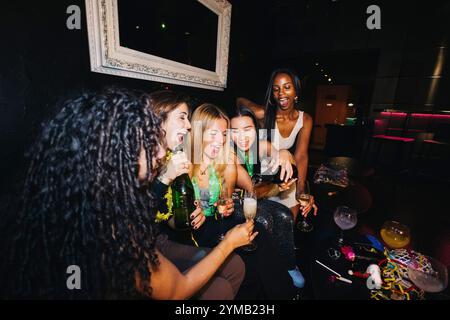 Un gruppo di amici che ridono e si godono la compagnia dell'altro mentre versano champagne in una vivace atmosfera da nightclub. Foto Stock