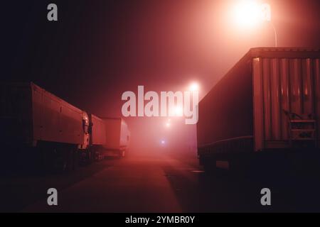 Parcheggio per semi-camion con veicoli e rimorchi nella notte nebbiosa, attenzione selettiva Foto Stock