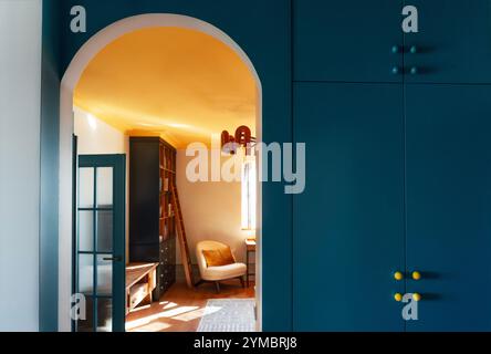 Interni eleganti e accoglienti del soggiorno. Una porta ad arco con una parete blu brillante e un guardaroba incorporato. Design a contrasto con il legno fu naturale Foto Stock