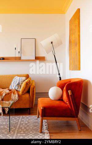 Primo piano di una morbida poltrona arancione realizzata in materiali naturali. Interni eleganti e moderni del soggiorno con soffitto giallo. Elegante piantana e. Foto Stock