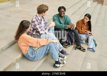 Gruppo di amici seduti sui gradini all'aperto e sorridenti Foto Stock