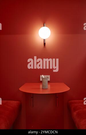 Ripresa verticale del tavolo in una vivace tonalità di rosso cabina caffè con design minimalista e lampada a parete, spazio fotocopie Foto Stock