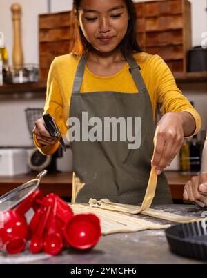 adolescente asiatica in cucina che prepara l'impasto con un taglierino per pasticceria, che si diverte a cucinare, a casa Foto Stock