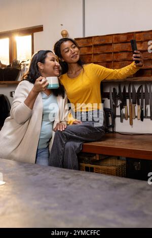 Adolescente asiatica che fa selfie con la nonna in cucina, a casa Foto Stock