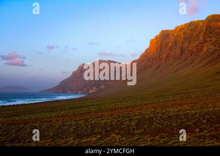 La luce del tramonto bagna le scogliere di Risco de Famara, affacciate sulla spiaggia di Famara a Lanzarote, Isole Canarie, Spagna. Foto Stock