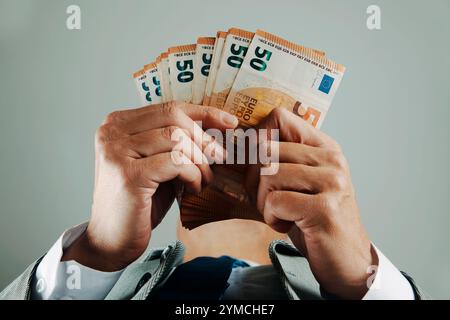 un uomo d'affari che indossa un abito, una camicia bianca e una cravatta, visto dal basso, conta alcune banconote in euro al chiuso Foto Stock