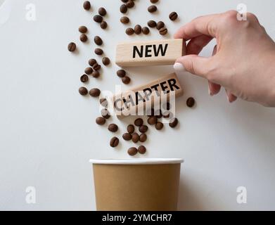 Nuovo simbolo di capitolo. Parola concettuale nuovo capitolo sui blocchi di legno. Mano d'affari. Splendido sfondo bianco con tazza di caffè. Business e nuovo capitolo Foto Stock
