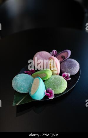 Dessert giapponese Mochi di colori diversi con sapori e ripieni diversi, su un piatto con fiori Foto Stock