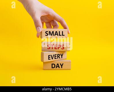 Simbolo piccoli passi ogni giorno. Blocchi di legno con parole piccoli passi ogni giorno. Bellissimo sfondo giallo. Mano d'affari. Business e piccoli passi Foto Stock