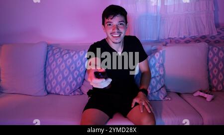 Giovane che guarda la televisione che sfoglia i canali con il telecomando a casa di notte Foto Stock
