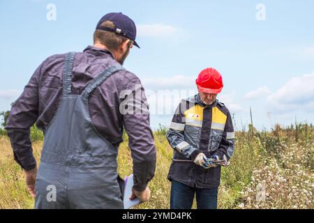 Due lavoratori in tuta con un palanchino in una zona rurale. Lavoratori municipali, meccanici e idraulici. Foto Stock