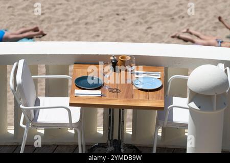 Prima dell'ora di pranzo, un elegante e vuoto caffè sulla spiaggia con tavoli serviti che aspettano gli ospiti nella soleggiata Biarritz, Paesi Baschi, Francia Foto Stock