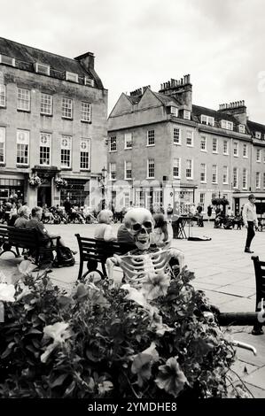 BATH, Regno Unito - 24 AGOSTO 2017: Turisti, gente del posto e divertente scheletro che si rilassano nella piazza nel centro di Bath nella giornata di sole. Foto in bianco e nero. Foto Stock