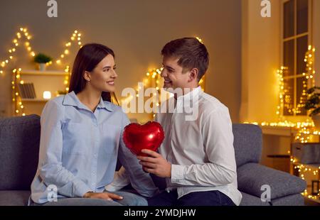 Il fidanzato sorprende la fidanzata con un cuore rosso sul divano Foto Stock