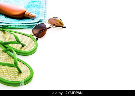 Accessori da spiaggia. Scarpe estive e asciugamano con occhiali da sole e lozione abbronzante su sfondo bianco Foto Stock