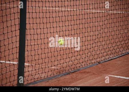 Palla da tennis gialla dietro la rete sul campo di argilla con sfondo sfocato Foto Stock