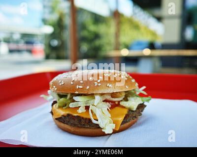 Un hamburger con lattuga e formaggio su un panino si trova su un vassoio rosso Il panino è tostato e la lattuga è fresca. L'hamburger è servito su un tovagliolo ed è pronto per essere consumato Foto Stock