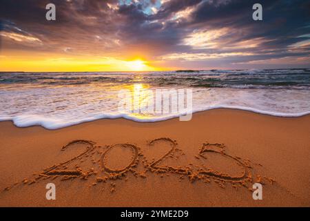 Happy New Year 2025, scritta sulla spiaggia. Testo scritto sulla spiaggia al sorgere del sole. Foto Stock