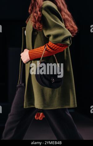 Splendidi dettagli alla moda di maglione arancione caldo, pantaloni neri, giacca verde e piccola borsa, tessuto alla moda da donna su sfondo nero Foto Stock