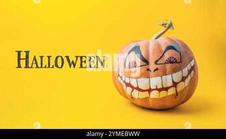 La zucca con un volto spaventoso dipinto su di essa è seduta su uno sfondo giallo con le parole Halloween scritte sotto di essa Foto Stock