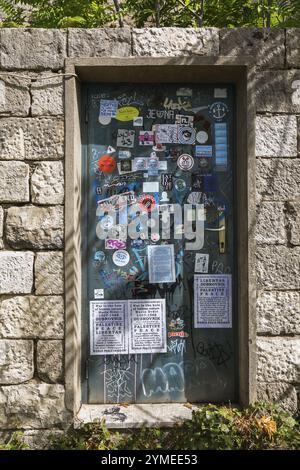 Vari messaggi politici, adesivi di dichiarazione, poster e graffiti sulla porta d'ingresso chiusa e chiusa a chiave incassata in un muro di pietra, Mount Srd, Dubrov Foto Stock