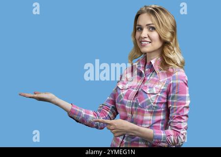 La giovane donna sorridente sta puntando allo spazio delle copie. Isolato su sfondo blu brillante Foto Stock