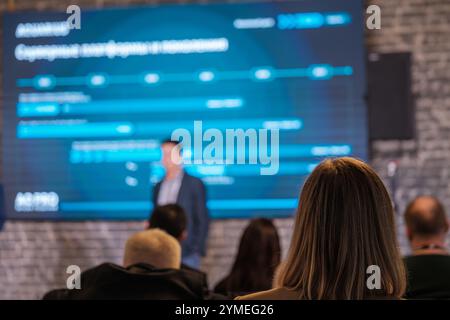 Professionista aziendale che offre presentazioni a un pubblico seduto, evidenziando i punti chiave su un grande schermo. Foto Stock