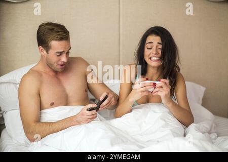 Coppia a letto con i telefoni. Due persone che giocano su smartphone. Prova e vinci Foto Stock