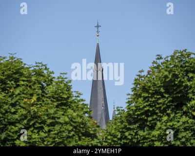 Guglia di una torre di chiesa si erge sopra le cime verdi degli alberi sotto un cielo blu, Weseke, muensterland, germania Foto Stock