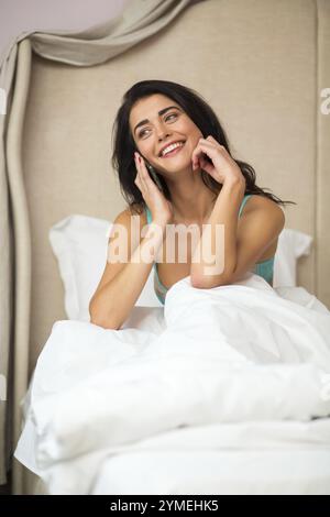 Donna a letto con il telefono. Ragazza che tiene lo smartphone e sorride. Ascolta la voce dell'amato Foto Stock