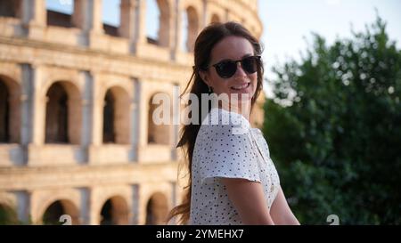 Donna allegra in occhiali da sole che posa giocosamente accanto al Colosseo di Roma Foto Stock