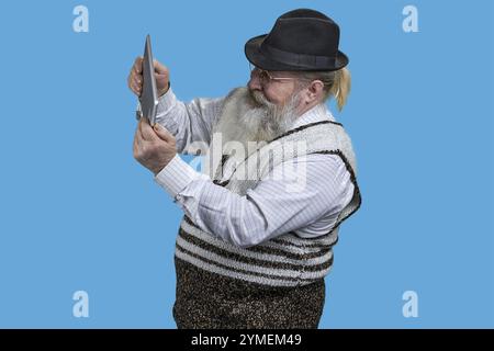 Ritratto di un uomo anziano entusiasta che gioca a videogame su un tablet pc. Isolato in blu Foto Stock