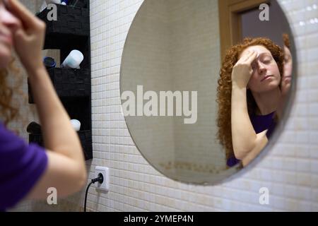 Giovane donna che rimuove il trucco con un panno di cotone nello specchio del bagno Foto Stock