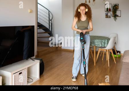 Donna che aspira il pavimento del soggiorno con un aspirapolvere cordless Foto Stock
