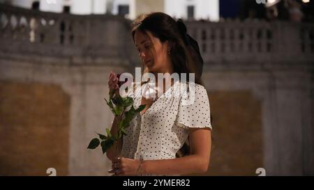 Donna premurosa con Rosa Rossa sotto il cielo notturno a Roma Foto Stock