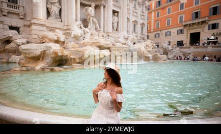 Donna in elegante abito bianco alla Fontana di Trevi, che cattura l'essenza dell'Italia Foto Stock