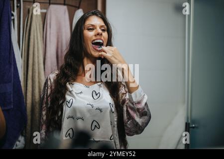 Giovane donna che pulisce i denti in un accogliente ambiente del bagno Foto Stock