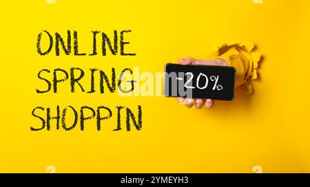 Persona che possiede un telefono cellulare con le parole Online Spring Shop scritte sullo schermo. L'immagine ha uno sfondo giallo e un alcalino bianco e nero Foto Stock